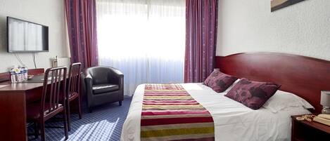 A hotel room with a bed, a desk, a chair, a television, and a window with curtains.