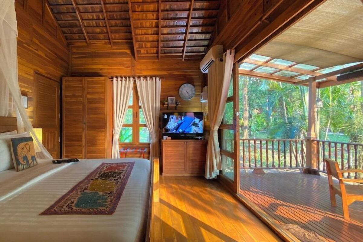 Eine Holzhütte mit einem Bett, einem Fernseher und einem Balkon mit Blick ins Freie.