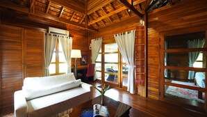 Ein Zimmer in einer Holzhütte mit einer Couch, einem Tisch mit einer Zeitschrift und einem Fenster mit Vorhängen.