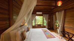 Ein Schlafzimmer in einer Holzhütte mit Bett, Vorhängen und Blick auf grüne Natur.