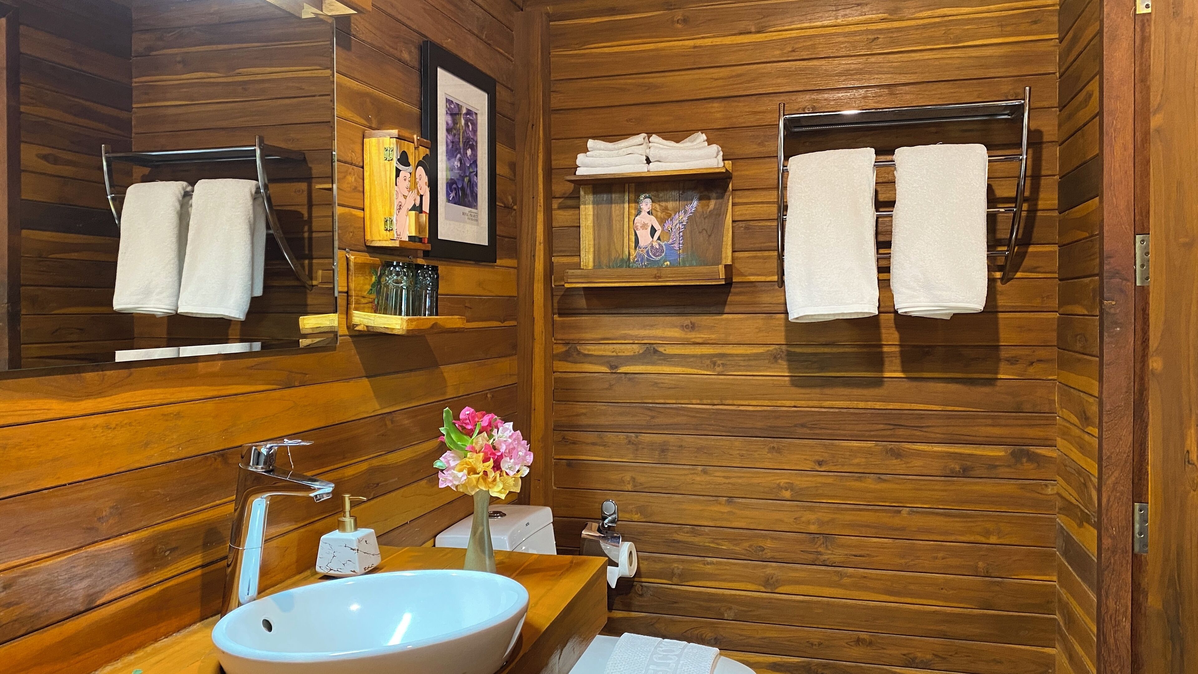 A wooden cabin-style bathroom with a large mirror, wooden shelves, a sink, and towels hanging on a rack.