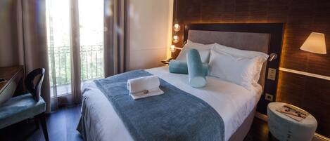 A hotel room with a bed, a chair, a bedside table, and a view of the outdoors.
