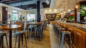 Um restaurante espaçoso com várias mesas e banquetas, piso de madeira e um bar com balcão e plantas decorativas.