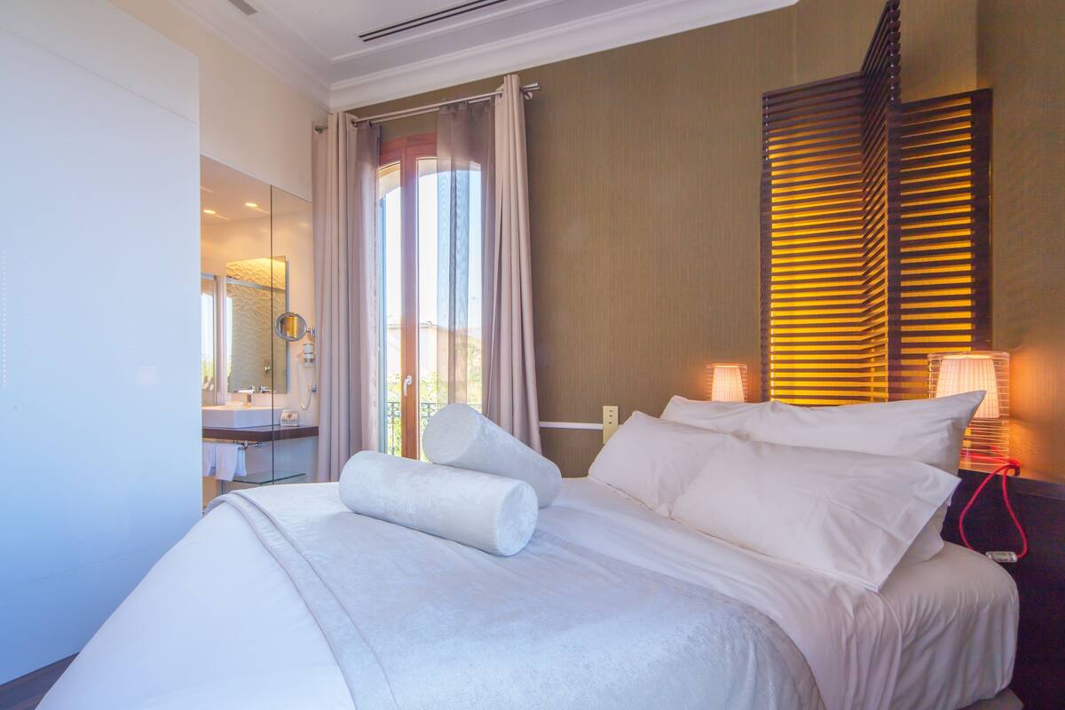 Habitación de hotel con una cama grande, un baño con cabina de ducha de vidrio y vistas al exterior.