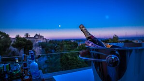 Uma garrafa de champanhe em um suporte para copos, com vista para um horizonte urbano e a lua ao fundo.