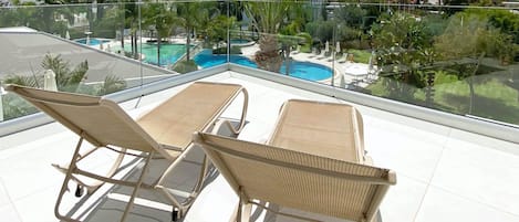 Un área de lounge en la azotea con dos sillones de mimbre, una piscina y vistas de los edificios y la vegetación circundantes.