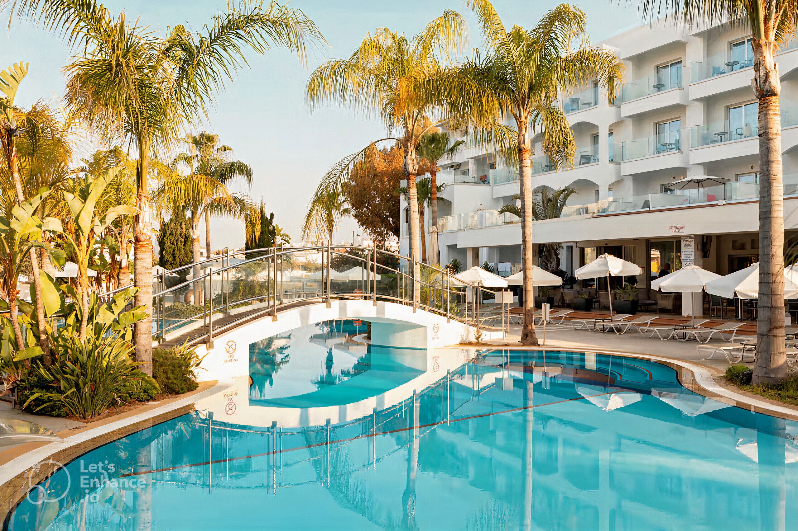 A pool area with a glass bridge, palm trees, and a building with balconies.