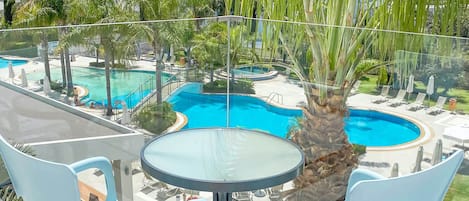 A glass-enclosed balcony with a pool, palm trees, and lounge chairs.