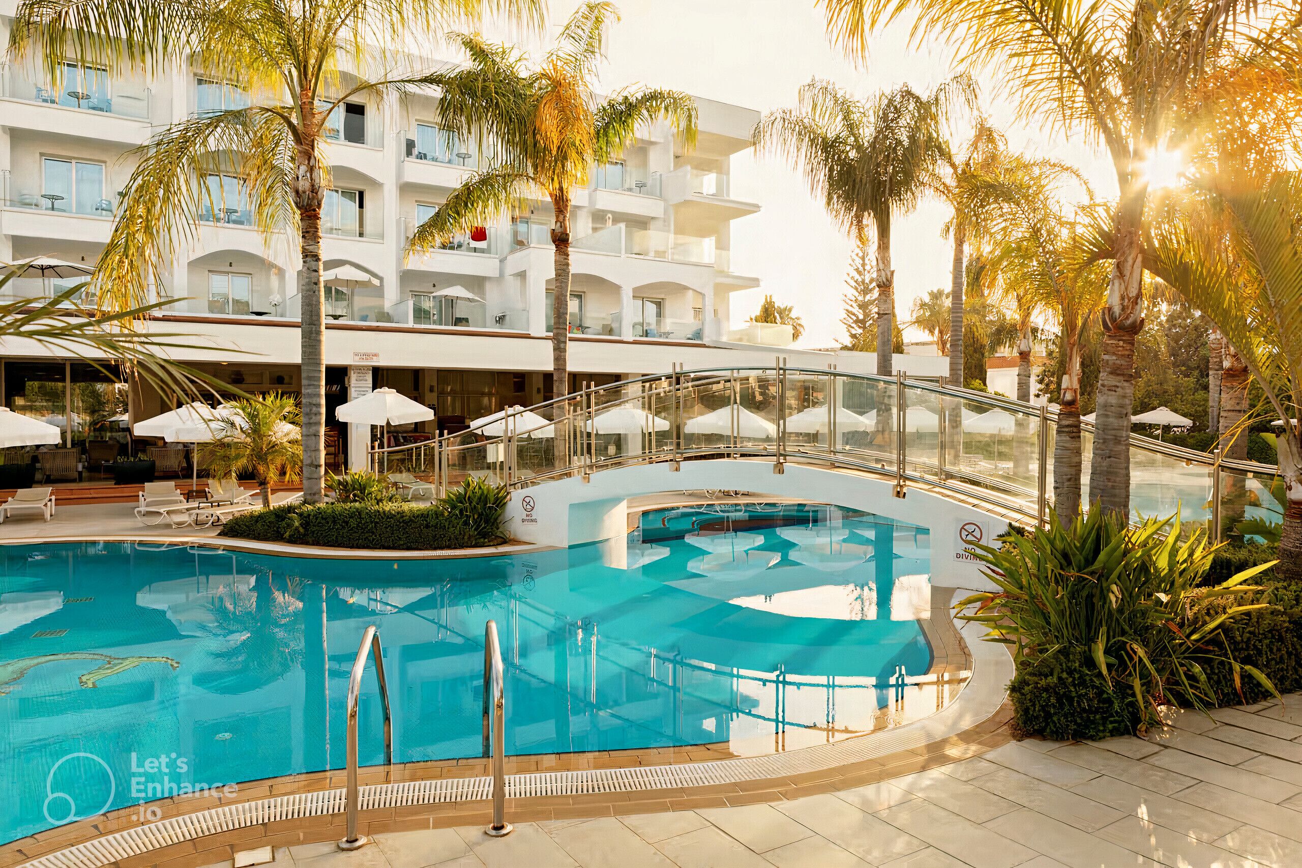 A swimming pool with a glass bridge, surrounded by palm trees and lounge chairs.