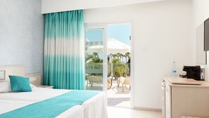 A hotel room with a bed, a desk, a chair, and a view of the outdoor area including a pool and umbrellas. - Anesis (Ayia Napa)