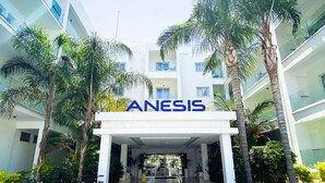 A modern building with a sign reading "ANESIS" at the entrance, surrounded by palm trees and a covered walkway. - Anesis (Ayia Napa)