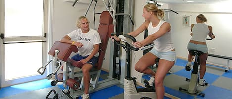 Ein Fitnessraum mit Trainingsgeräten, einem Spiegel und einer Tür.