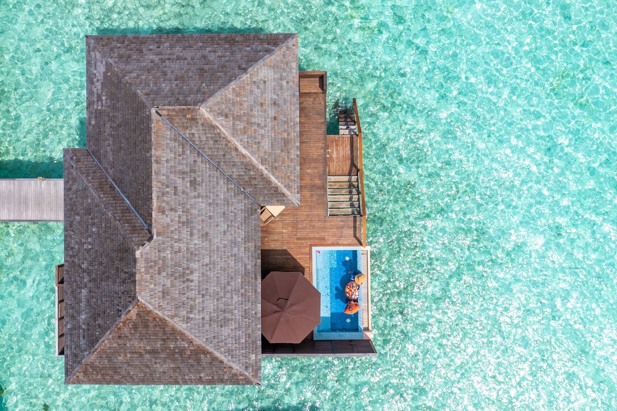 An aerial view of a resort with a wooden deck, a swimming pool, and clear turquoise water.
