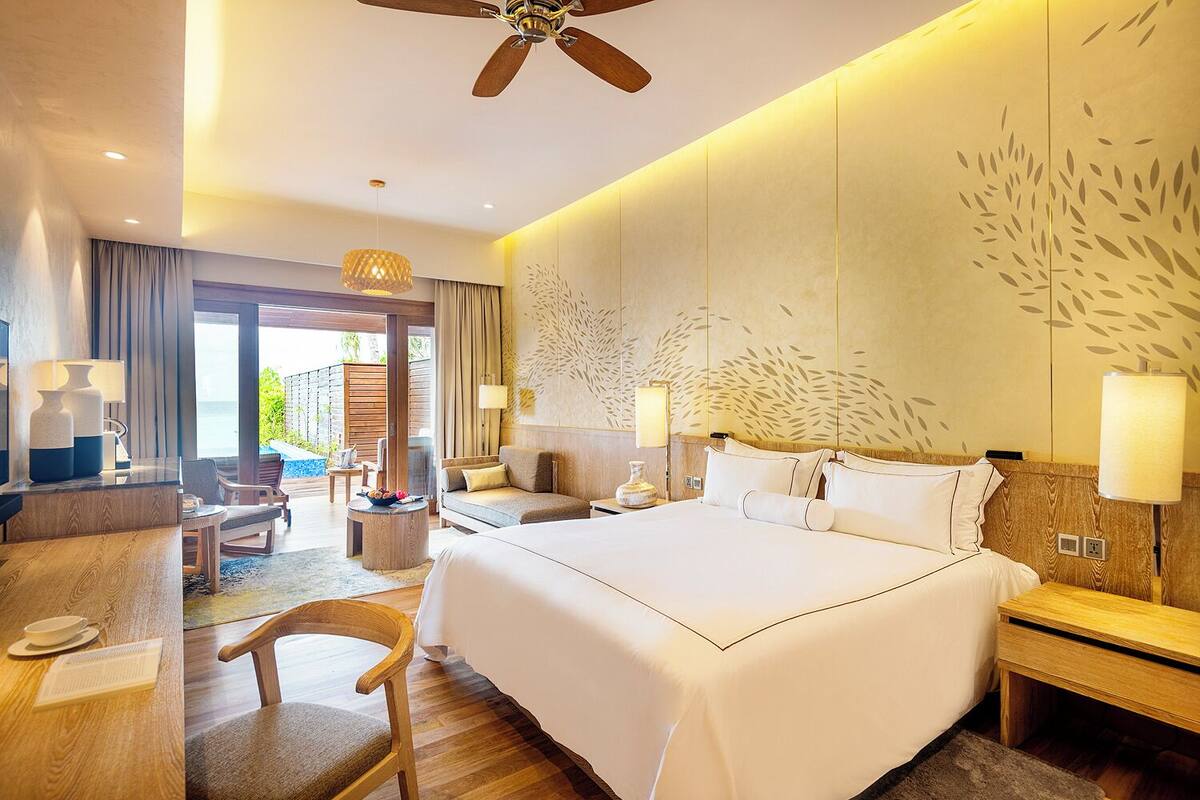 A hotel room with a large bed, a desk with a chair, a sofa, and a view of the outdoors.