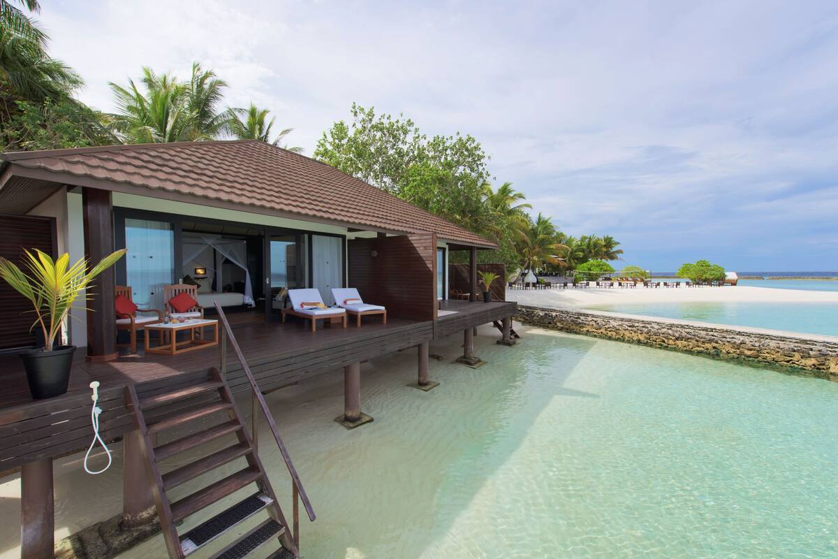 A beachfront villa with a wooden deck, lounge chairs, and a view of the ocean.