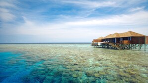 Ein Bungalow auf Stelzen über dem Wasser mit freiem Blick auf das türkisfarbene Meer und das darunterliegende Korallenriff.