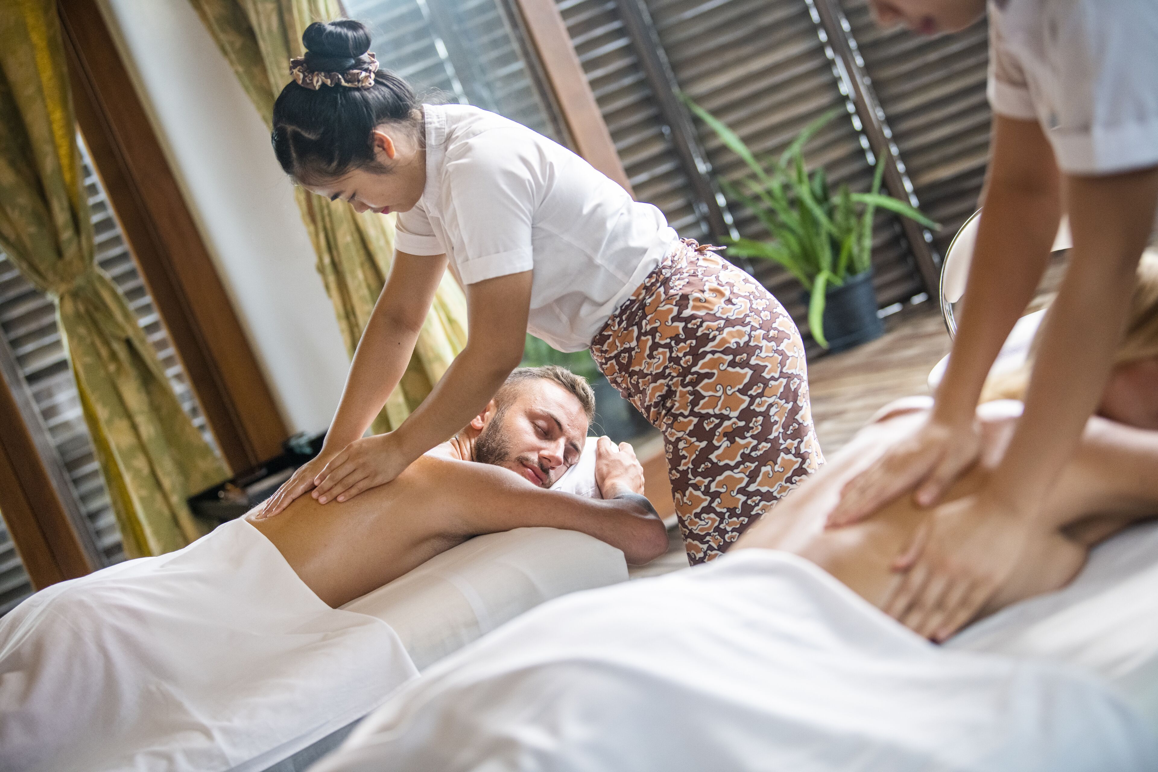 A massage therapy session in a room with wooden beams and a potted plant.
