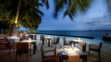 A beachfront restaurant with tables and chairs set up on the sand, overlooking the ocean.
