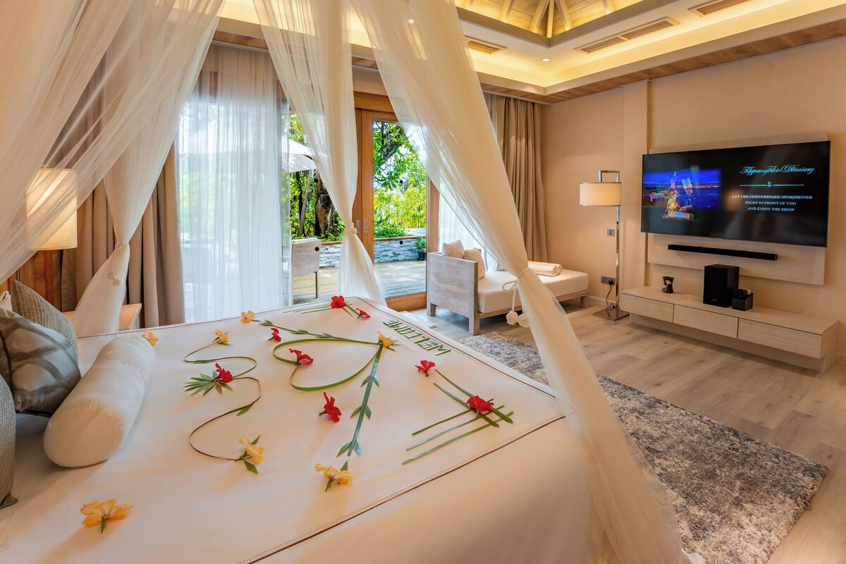 A bedroom with a canopy bed, a TV, and a view of greenery outside.