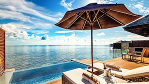 Ein Pool ohne Ende mit Holzterrasse, Liegestühlen, einem großen Sonnenschirm und Blick auf den Ozean.