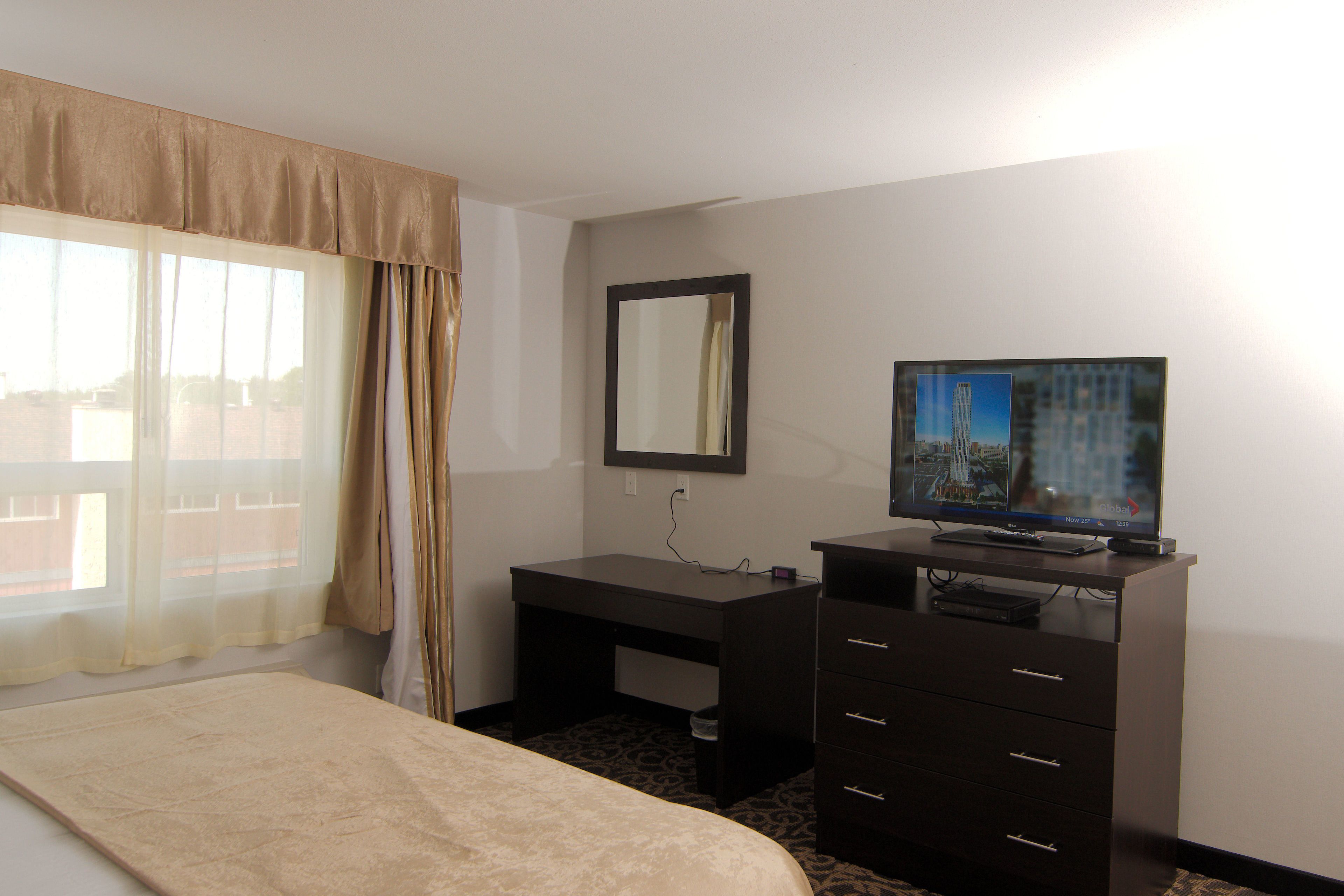 Ein Hotelzimmer mit Bett, Schreibtisch, Fernseher und einem Fenster mit Vorhängen.