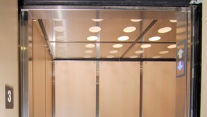 An elevator with a metallic interior, a handrail, and a carpeted floor. - Paradise Inn & Kitchenette Suites (Redwater)