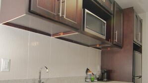 A kitchen with dark wooden cabinets, a stainless steel microwave, and a double sink. - Paradise Inn & Kitchenette Suites (Redwater)
