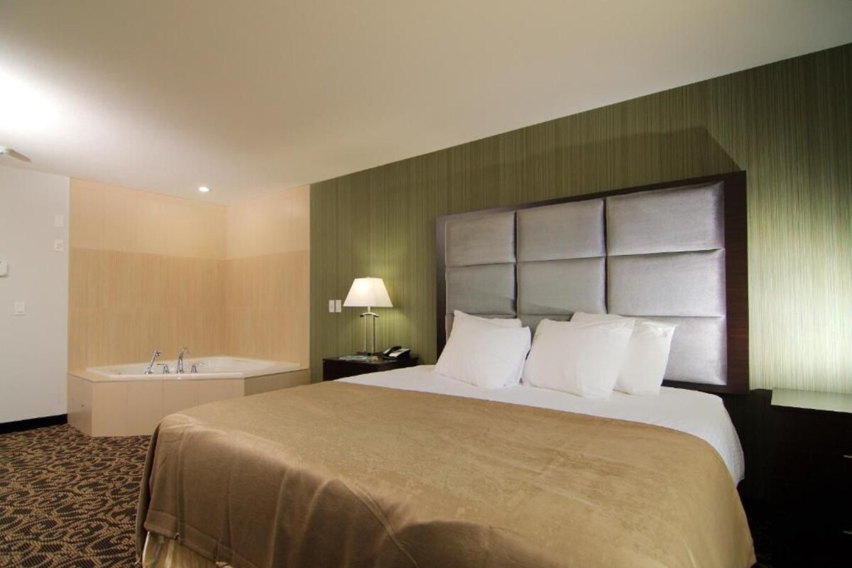 A hotel room with a large bed, a separate bathroom with a bathtub, and a nightstand with a lamp.