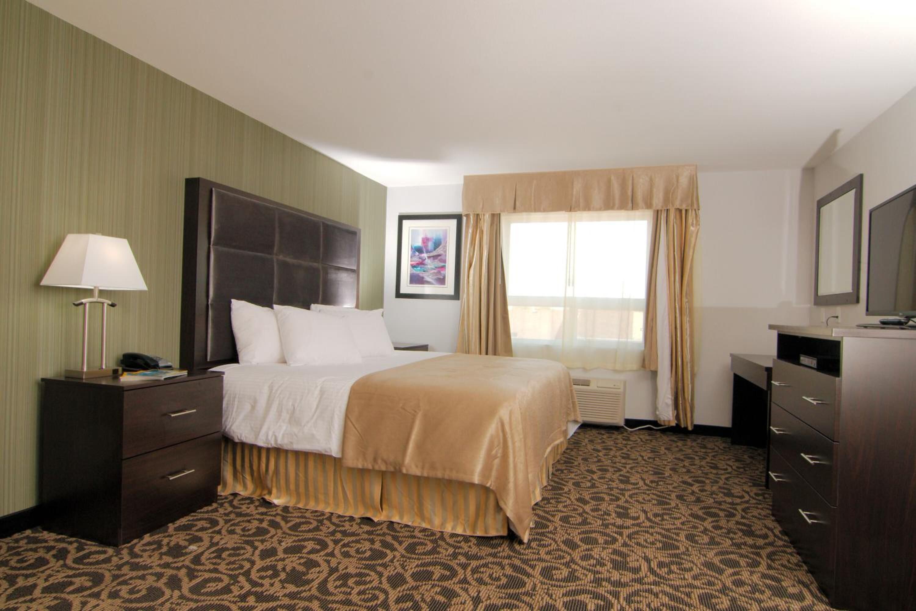 A hotel room with a bed, a desk, a lamp, a framed picture, and a window with curtains.