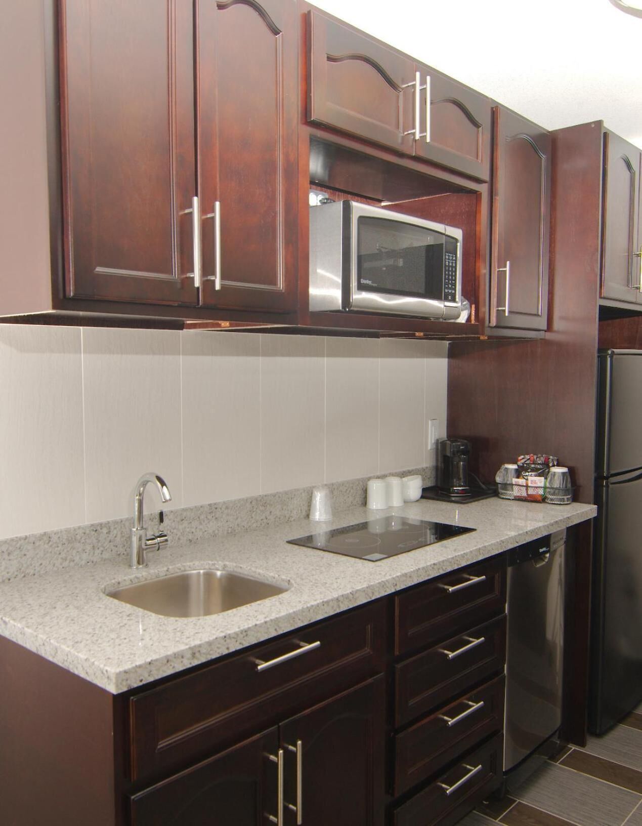 A kitchen with dark wooden cabinets, stainless steel appliances, a granite countertop, and a built-in dishwasher.
