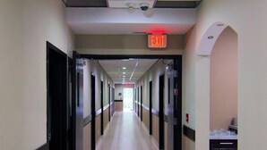 A long, narrow hallway with doors on both sides, a visible exit sign, and a ceiling with recessed lighting. - Paradise Inn & Kitchenette Suites (Redwater)