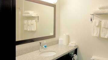 A hotel bathroom with a large mirror, two sinks, a toilet, and a towel rack.