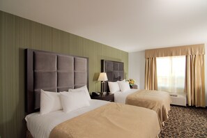 A hotel room with two beds, a large headboard, a bedside table with a lamp, and a window with curtains. - Paradise Inn & Kitchenette Suites (Redwater)