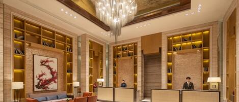 A hotel lobby with a reception desk, seating area, and bookshelves.