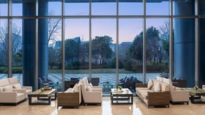 Un hall d’entrée spacieux, doté de grandes fenêtres, de mobilier moderne et offrant une vue sur un jardin et un élément décoratif aquatique.