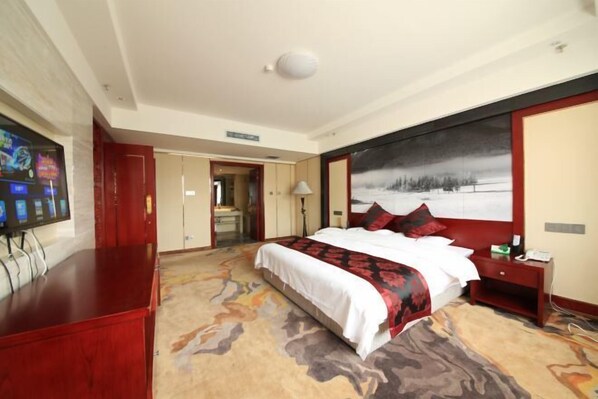 A hotel room with a large bed, a TV, a desk, and a painting on the wall.