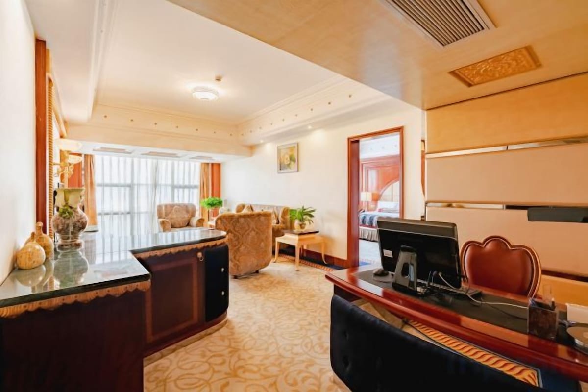 A hotel room with a desk, a chair, a sofa, and a large window.