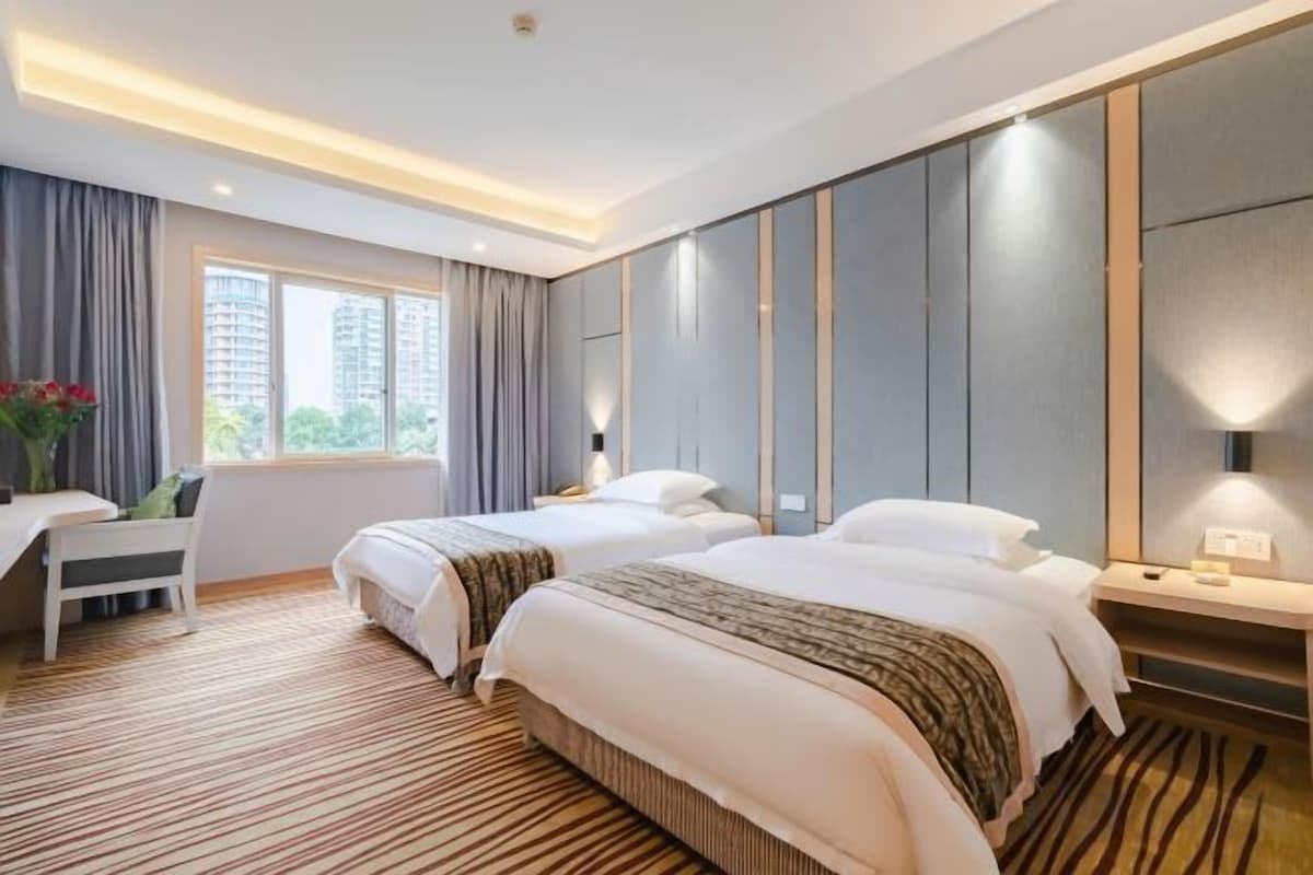 A hotel room with two beds, a desk, and a view of the city.