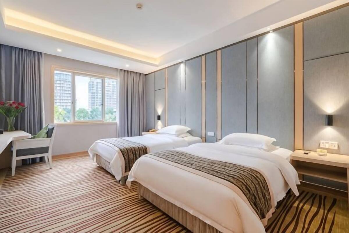 A hotel room with two beds, a desk, a chair, and a large window.