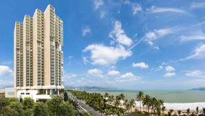 Un hôtel de grande hauteur, avec de nombreux étages, une vue sur la plage et une route bordée de palmiers.