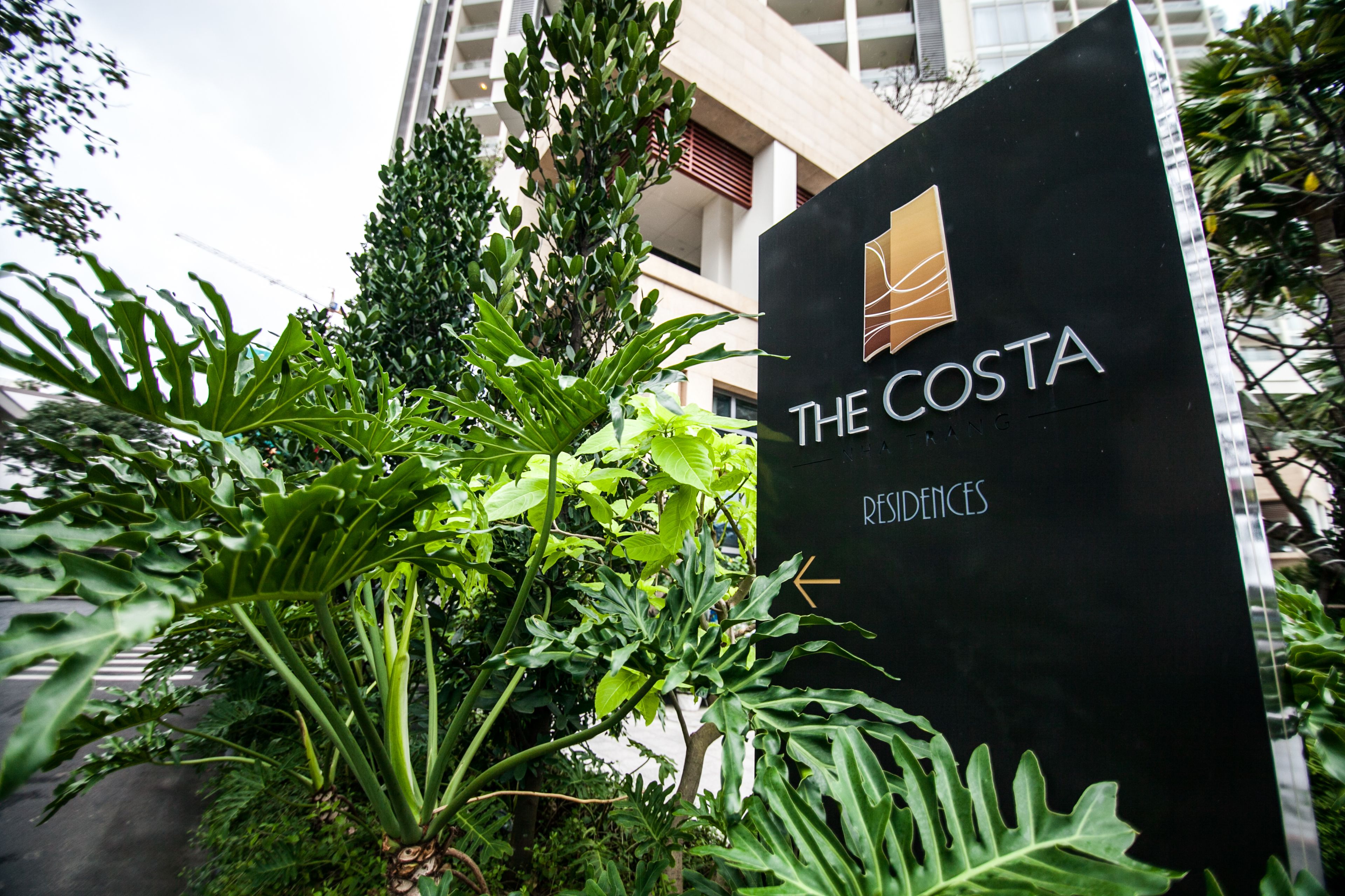 A sign for "The Costa Residences" with a modern building in the background.
