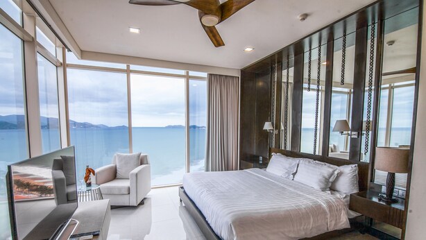 Une chambre d’hôtel moderne dotée d’un grand lit, d’une télévision, d’un canapé et offrant une vue sur la mer.