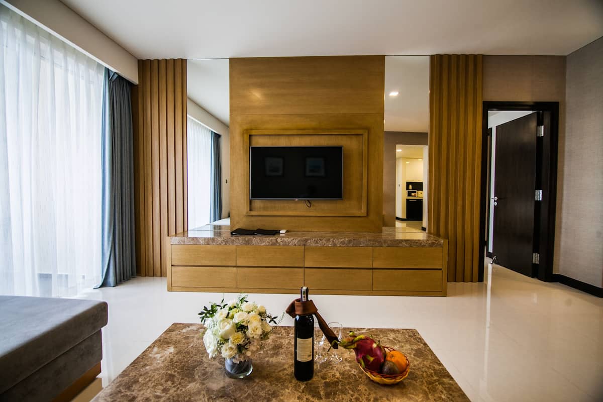 Een moderne woonkamer met een flatscreen televisie bevestigd aan een houten wand, een bank, een salontafel met een fles wijn, glazen en een schaal fruit.