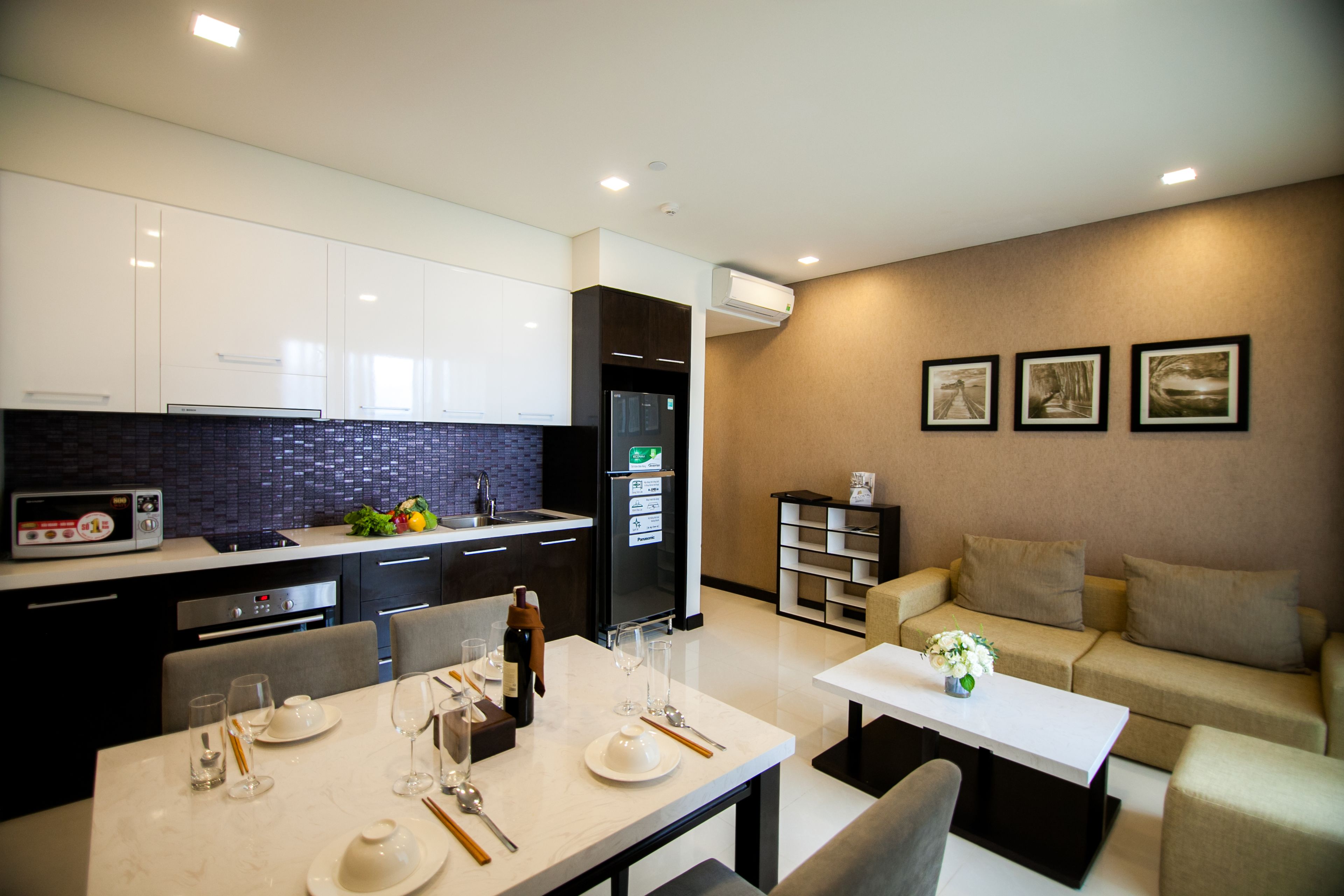 Une cuisine moderne avec des meubles blancs, un réfrigérateur noir et un coin repas comprenant une table et des chaises blanches.