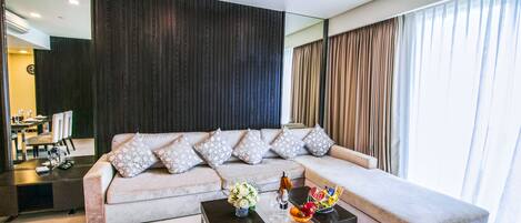 A modern living room with a sofa, coffee table, and a dining area in the background.
