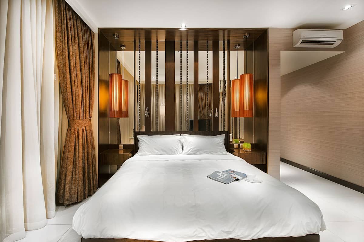 Een moderne hotelkamer met een groot bed, een houten hoofdeinde en twee hanglampen.