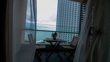 A balcony with a table and chairs, overlooking a cityscape and the ocean.