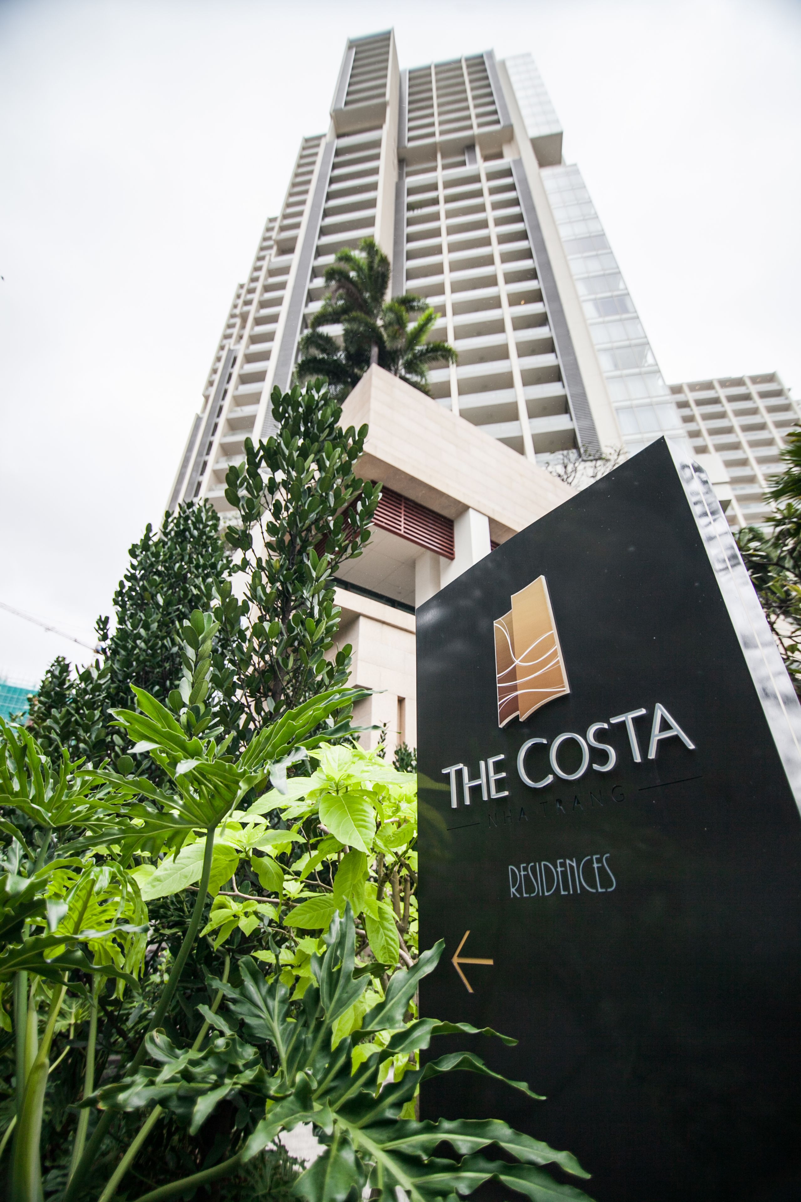 Señal de 'The Costa Residences' con un edificio moderno al fondo.