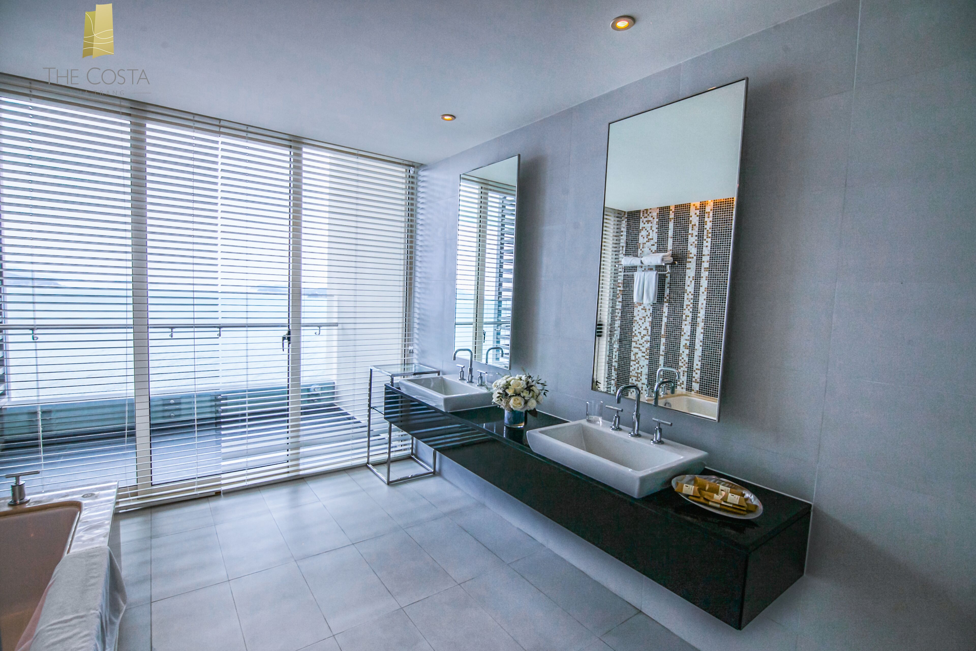 Ein modernes Badezimmer mit zwei Waschbecken, einem großen Spiegel und Blick durch raumhohe Fenster.