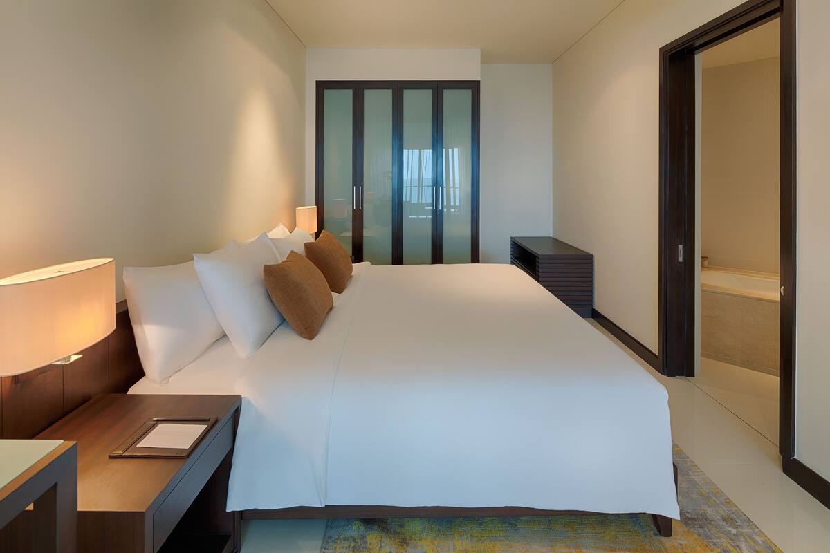 Een hotelkamer met een groot bed, een nachtkastje, een bureau en een schuifdeur naar een badkamer.